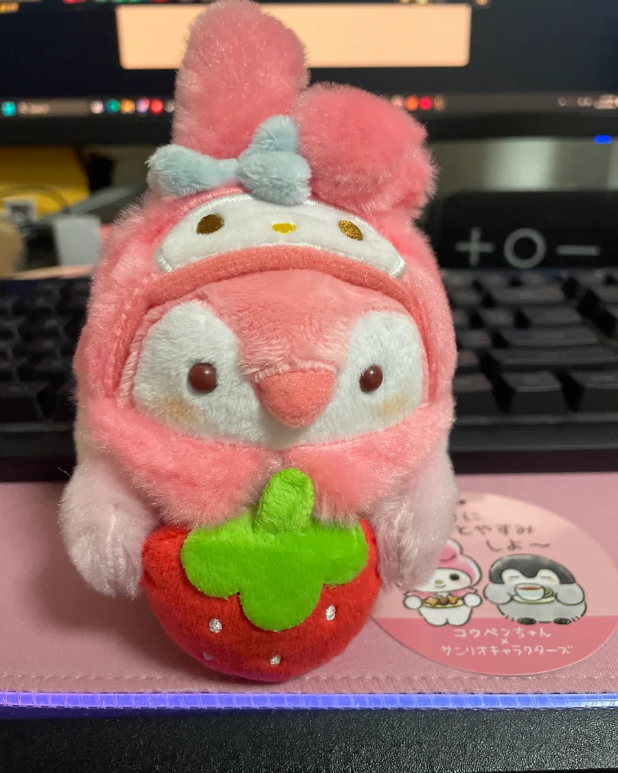 A pink penguin plush in a My Melody hood holding a strawberry